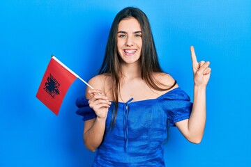 Young brunette teenager holding albania flag smiling with an idea or question pointing finger with happy face, number one