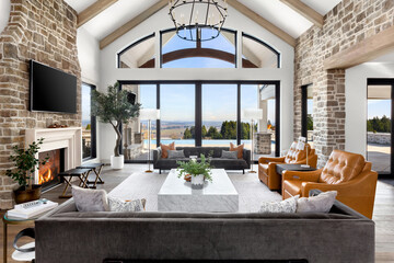 Beautiful living room in new luxury home. Features vaulted ceilings with wood beams, stone accents, chandelier, fireplace with roaring fire, and gorgeous exterior view with infinity pool and valley.