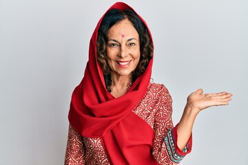 Middle age hispanic woman wearing tradition sherwani saree clothes smiling cheerful presenting and pointing with palm of hand looking at the camera.