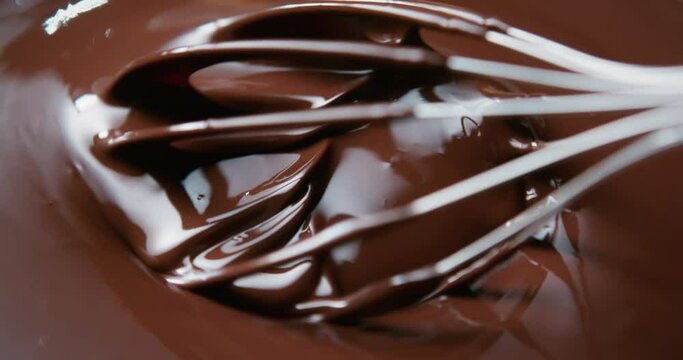 Close-up chocolatier mixing melted liquid chocolate with steel whisk. Hot chocolate mix and swirl in bowl. Cooking handmade chocolate dessert and candies. Confectionery concept
