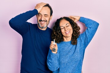 Middle age couple of hispanic woman and man holding keys of new home smiling confident touching hair with hand up gesture, posing attractive and fashionable