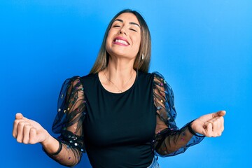 Fototapeta premium Young hispanic woman wearing casual clothes very happy and excited doing winner gesture with arms raised, smiling and screaming for success. celebration concept.