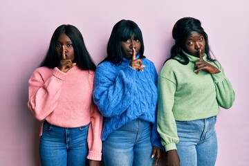 Three young african american friends wearing wool winter sweater asking to be quiet with finger on lips. silence and secret concept.