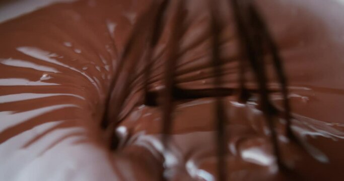 Close-up chocolatier mixing melted liquid chocolate with steel whisk. Hot chocolate mix and swirl in bowl. Cooking handmade chocolate dessert and candies. Confectionery concept