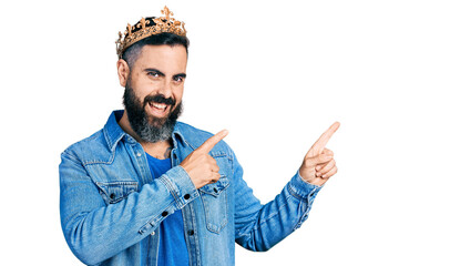 Hispanic man with beard wearing king crown smiling and looking at the camera pointing with two hands and fingers to the side.