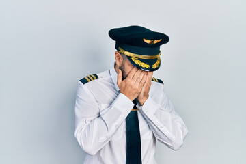 Young hispanic man wearing airplane pilot uniform with sad expression covering face with hands while crying. depression concept. © Krakenimages.com