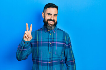 Young hispanic man wearing casual clothes smiling with happy face winking at the camera doing victory sign. number two.