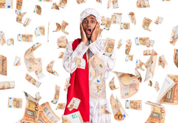 African handsome man wearing tradition sherwani saree clothes afraid and shocked, surprise and amazed expression with hands on face