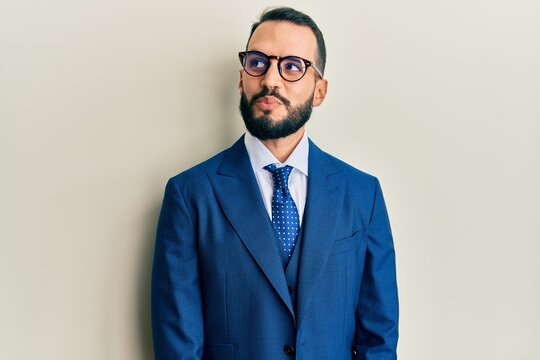 Young man with beard wearing business suit and tie smiling looking to the side and staring away thinking.