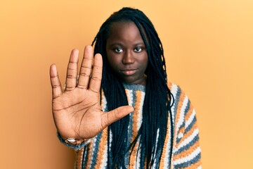 Young black woman with braids wearing casual winter sweater doing stop sing with palm of the hand. warning expression with negative and serious gesture on the face.