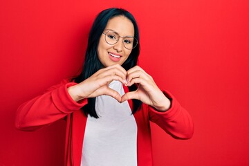 Beautiful hispanic woman with nose piercing wearing casual look and glasses smiling in love doing heart symbol shape with hands. romantic concept.