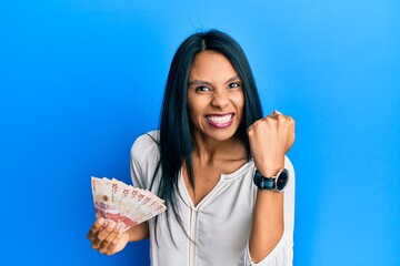 Young african american woman holding 10 colombian pesos banknotes angry and mad raising fist frustrated and furious while shouting with anger. rage and aggressive concept. - obrazy, fototapety, plakaty
