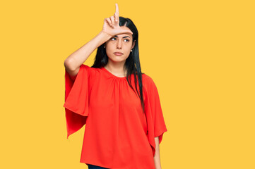 Beautiful young woman wearing casual clothes making fun of people with fingers on forehead doing...