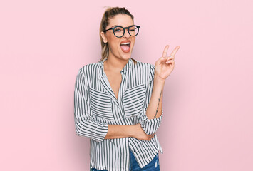 Young caucasian woman wearing business shirt and glasses smiling with happy face winking at the...