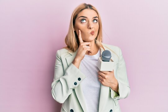 Young caucasian woman holding reporter microphone serious face thinking about question with hand on chin, thoughtful about confusing idea