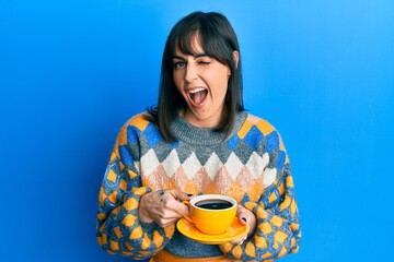 Young hispanic woman drinking a cup of coffee winking looking at the camera with sexy expression, cheerful and happy face.