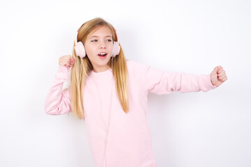 Obraz na płótnie Canvas beautiful caucasian little girl wearing pink hoodie over white background, dancing and listening music with headphones.