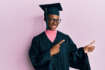 Young african american girl wearing graduation cap and ceremony robe smiling and looking at the...