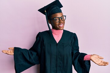 Young african american girl wearing graduation cap and ceremony robe smiling showing both hands...