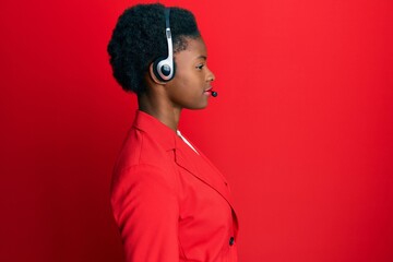 Young african american girl wearing call center agent headset looking to side, relax profile pose...