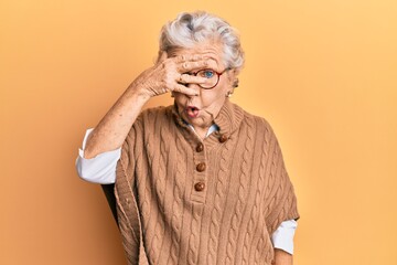 Senior grey-haired woman wearing casual clothes and glasses peeking in shock covering face and eyes...