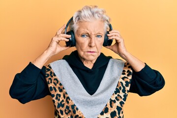 Senior grey-haired woman listening to music using headphones skeptic and nervous, frowning upset...