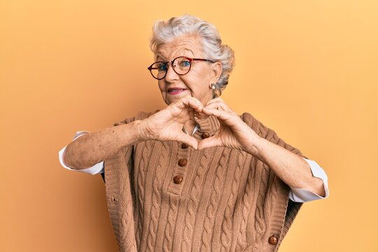 Senior grey-haired woman wearing casual clothes and glasses smiling in love doing heart symbol shape with hands. romantic concept.