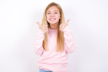 Optimistic beautiful caucasian little girl wearing pink hoodie over white background showing thumbs up with positive emotions. Quality and recommendation concept.