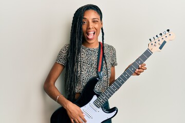 African american woman playing electric guitar winking looking at the camera with sexy expression,...