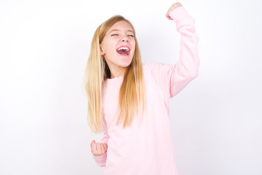 Attractive Beautiful Caucasian Little Girl Wearing Pink Hoodie Over White Background Celebrating A Victory Punching The Air With His Fists And A Beaming Toothy Smile