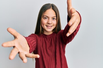 Beautiful brunette little girl wearing casual sweater looking at the camera smiling with open arms for hug. cheerful expression embracing happiness.