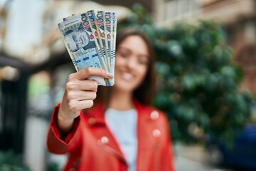 Young hispanic woman smiling happy holding peruvian sol banknotes at the city. - obrazy, fototapety, plakaty