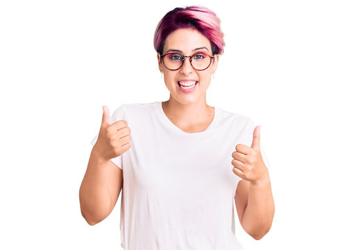 Young beautiful woman with pink hair wearing casual clothes and glasses success sign doing positive gesture with hand, thumbs up smiling and happy. cheerful expression and winner gesture.