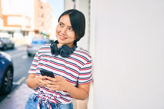 Young latin girl smiling happy using smartphone and headphones at the city