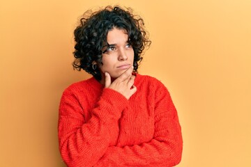 Fototapeta na wymiar Young hispanic woman with curly hair wearing casual winter sweater thinking worried about a question, concerned and nervous with hand on chin