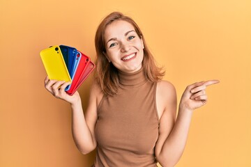 Young caucasian woman holding smartphone case smiling happy pointing with hand and finger to the...