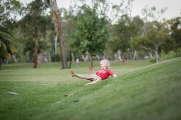 Little boy lying on beautiful grassy green hill and rolling down. Nature fun with children.