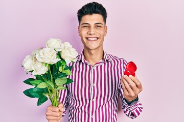 Young hispanic man holding bouquet of flowers and wedding ring smiling with a happy and cool smile on face. showing teeth.