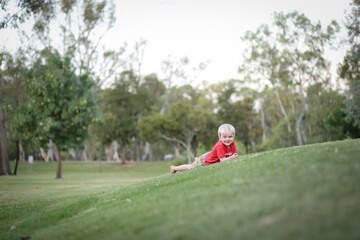 Fototapeta premium Little boy lying on beautiful grassy green hill and rolling down. Nature fun with children.