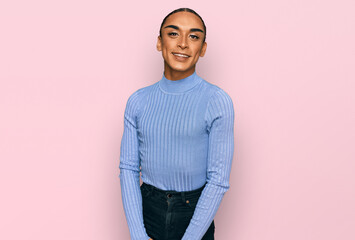 Hispanic transgender man wearing make up and long hair wearing casual clothes looking positive and happy standing and smiling with a confident smile showing teeth