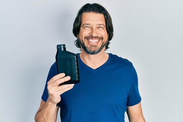 Fototapeta na wymiar Middle age caucasian man holding motor oil bottle looking positive and happy standing and smiling with a confident smile showing teeth