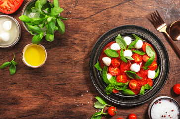 Summer italian salad Caprese with red tomatoes and mozzarella cheese with green basil leaves and olive oil dressing. Top view, wooden table