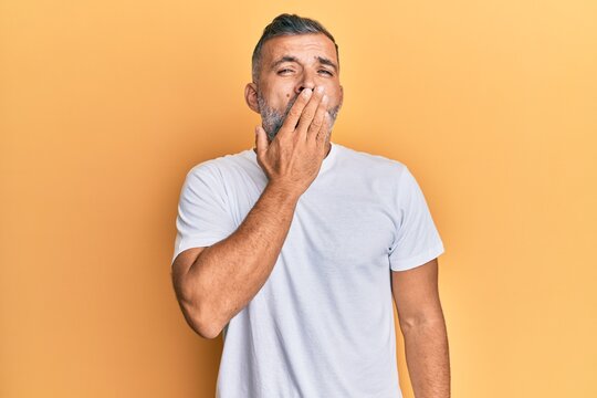 Middle age handsome man wearing casual white tshirt bored yawning tired covering mouth with hand. restless and sleepiness.