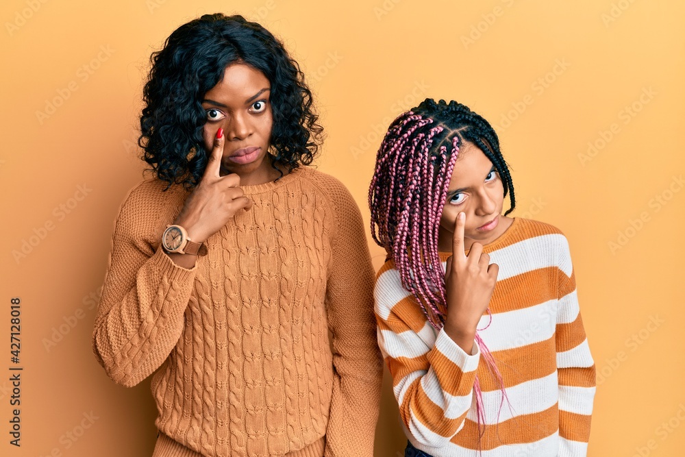 Poster beautiful african american mother and daughter wearing wool winter sweater pointing to the eye watch