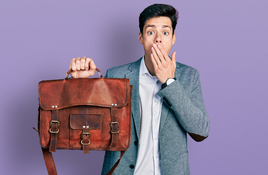 Young hispanic man holding business bag covering mouth with hand, shocked and afraid for mistake. surprised expression