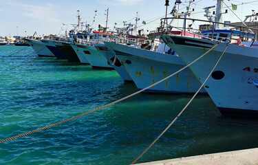 Naklejka premium Barche da pesca in porto all’attracco riflessi del sole nel mare verde e gomene tese