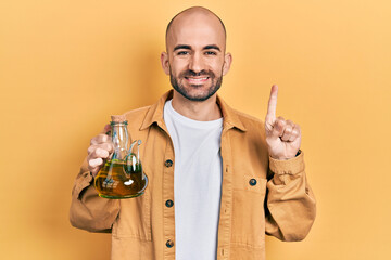Young bald man holding olive oil can smiling with an idea or question pointing finger with happy...