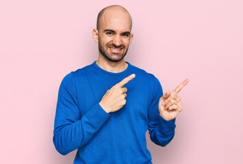 Young hispanic man wearing casual clothes smiling and looking at the camera pointing with two hands and fingers to the side.