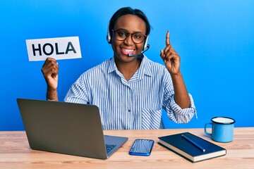 Young african woman wearing operator headset holding hola word smiling with an idea or question pointing finger with happy face, number one © Krakenimages.com