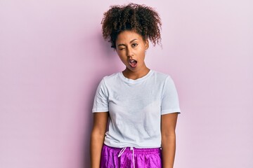 Beautiful african american woman with afro hair wearing sportswear winking looking at the camera with sexy expression, cheerful and happy face.